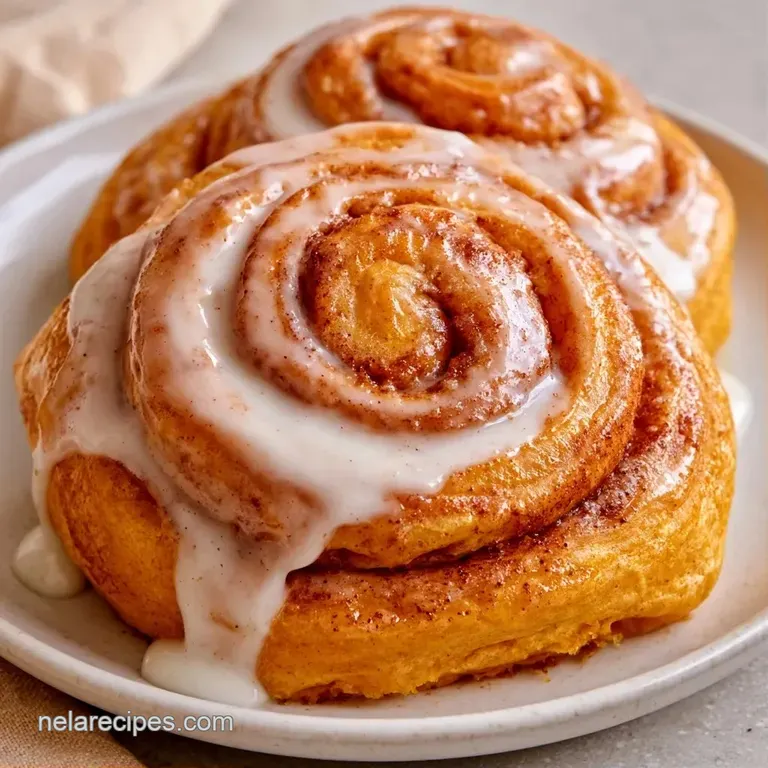 Three fluffy orange-hued rolls on a white ceramic plate, drizzled with glossy glaze and a dash of cinnamon.